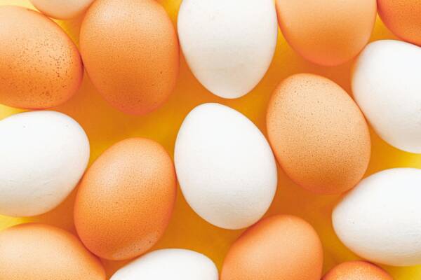 Top view of brown and white eggs arranged on a vibrant yellow surface, offering a minimalistic food pattern.