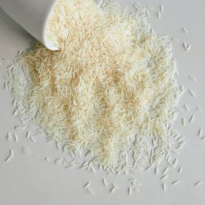 High-angle shot of uncooked white rice spilling from a ceramic cup onto a smooth surface.