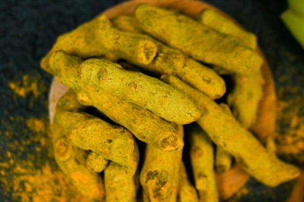 Vibrant close-up of organic turmeric roots displayed on a wooden plate, perfect for cooking and health inspiration.